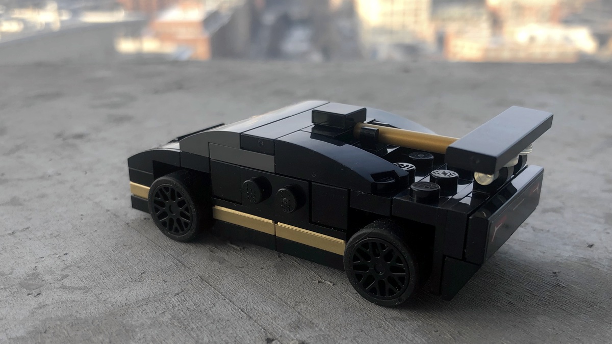 Side on with the mini LEGO Lamborghini showing the gold features and the wheels protruding from the body. The non transparent windscreen looks strange from this angle too.